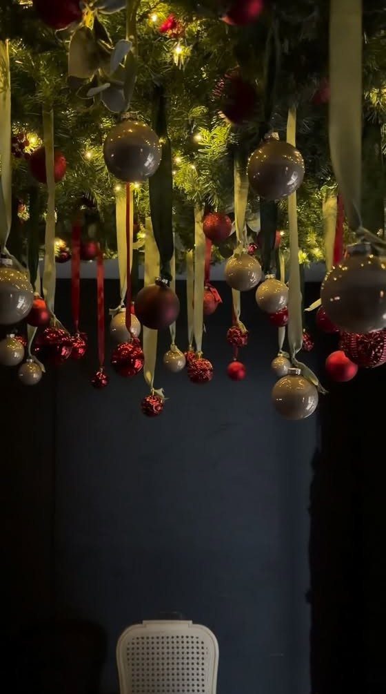 Christmas ornaments hanging from a ceiling of pine branches with warm fairy lights.