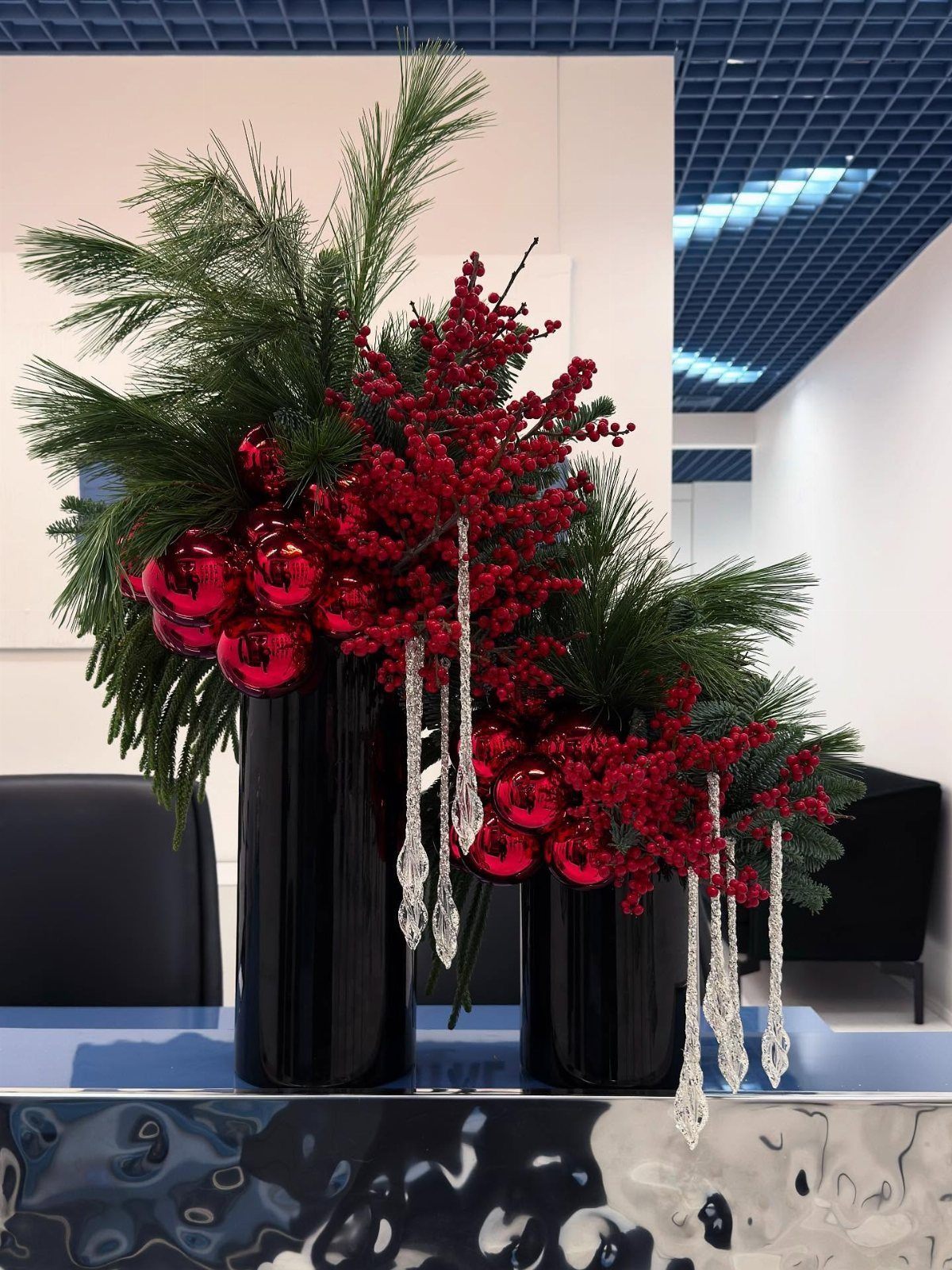 Festive holiday arrangement with red berries and ornaments in black vases in office