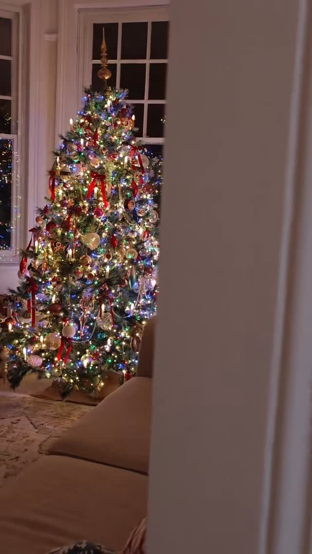 Narrow Christmas tree decorated with colorful lights and red ribbons in a living room