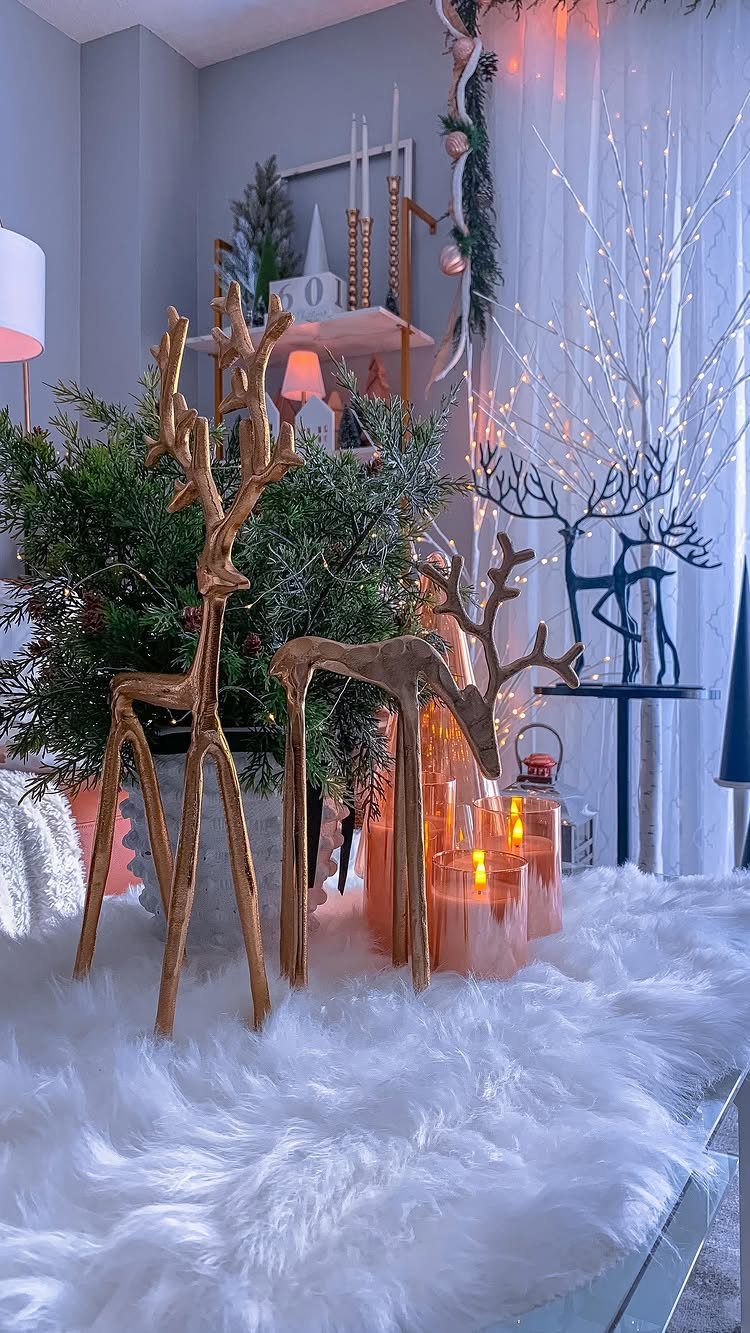 Gold reindeer figurines on white faux fur with glowing candles and festive greenery.