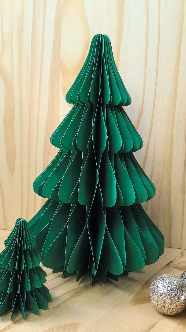 Green 3D paper Christmas trees with pleated layers on a wooden surface.