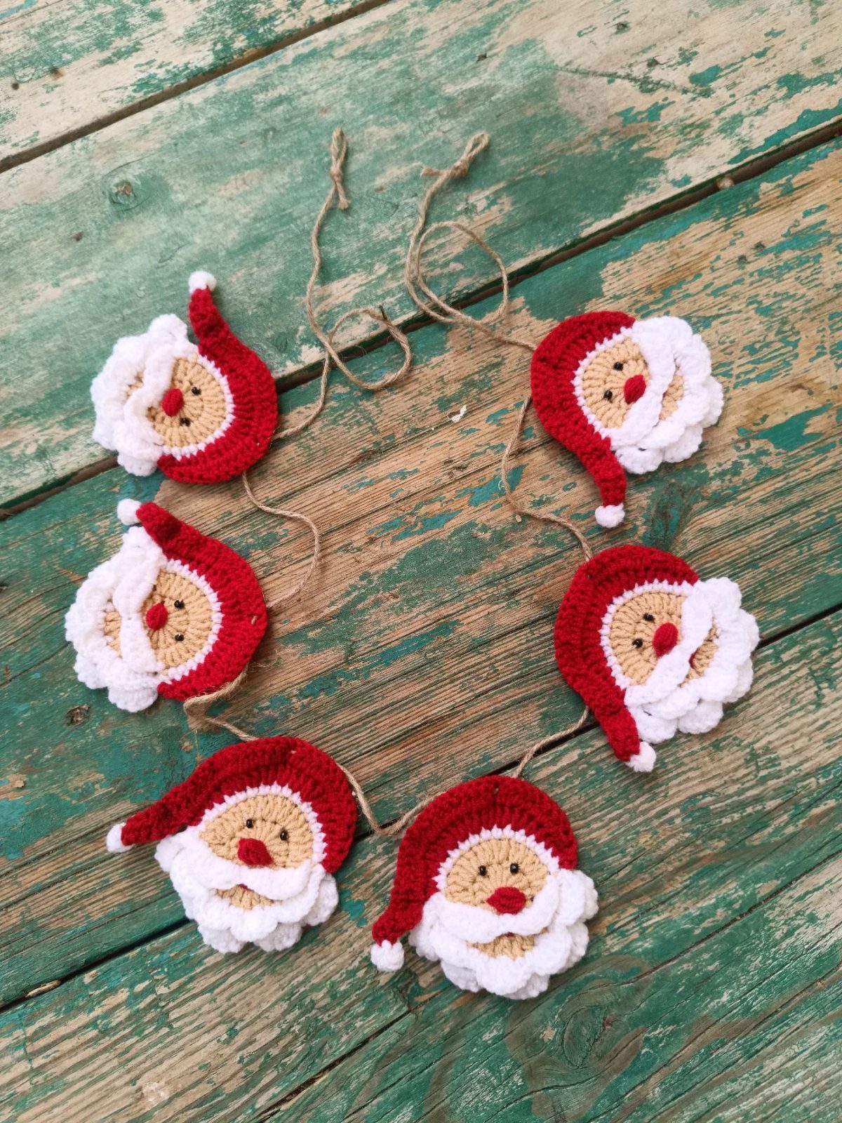 Crocheted Santa Claus head garland resting on a rustic green wooden background.