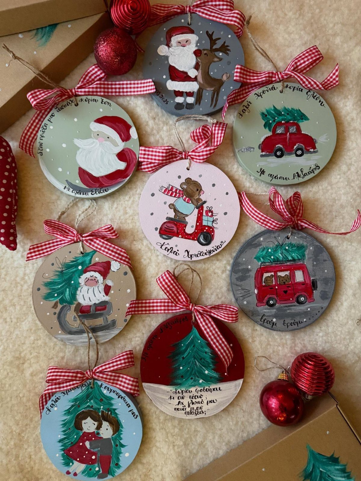 Hand-painted round Christmas ornaments with red checkered ribbons on a white fluffy background.