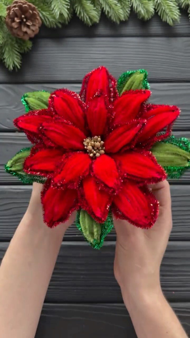 Handmade red glittery poinsettia flower held by two hands against dark wood background