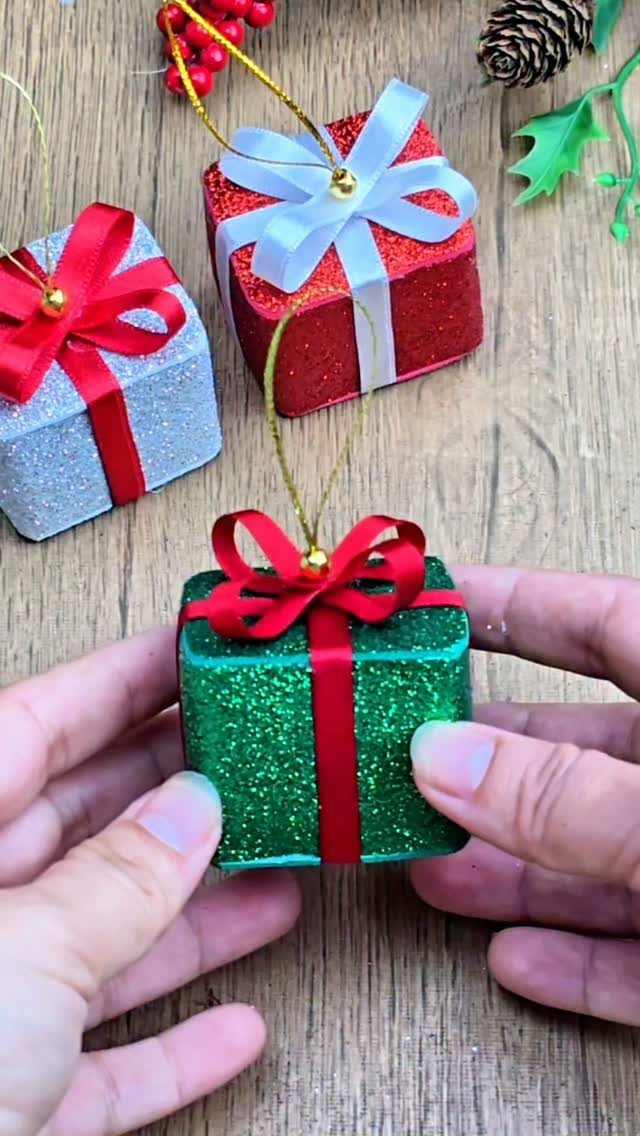 Glittery green gift ornament held by hands on a wooden surface with decorations.