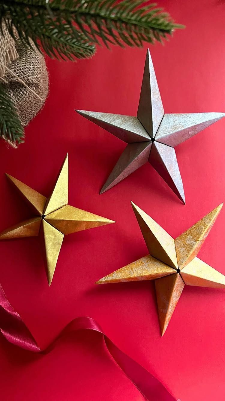 Three 3D folded paper stars in metallic colors on a red background.