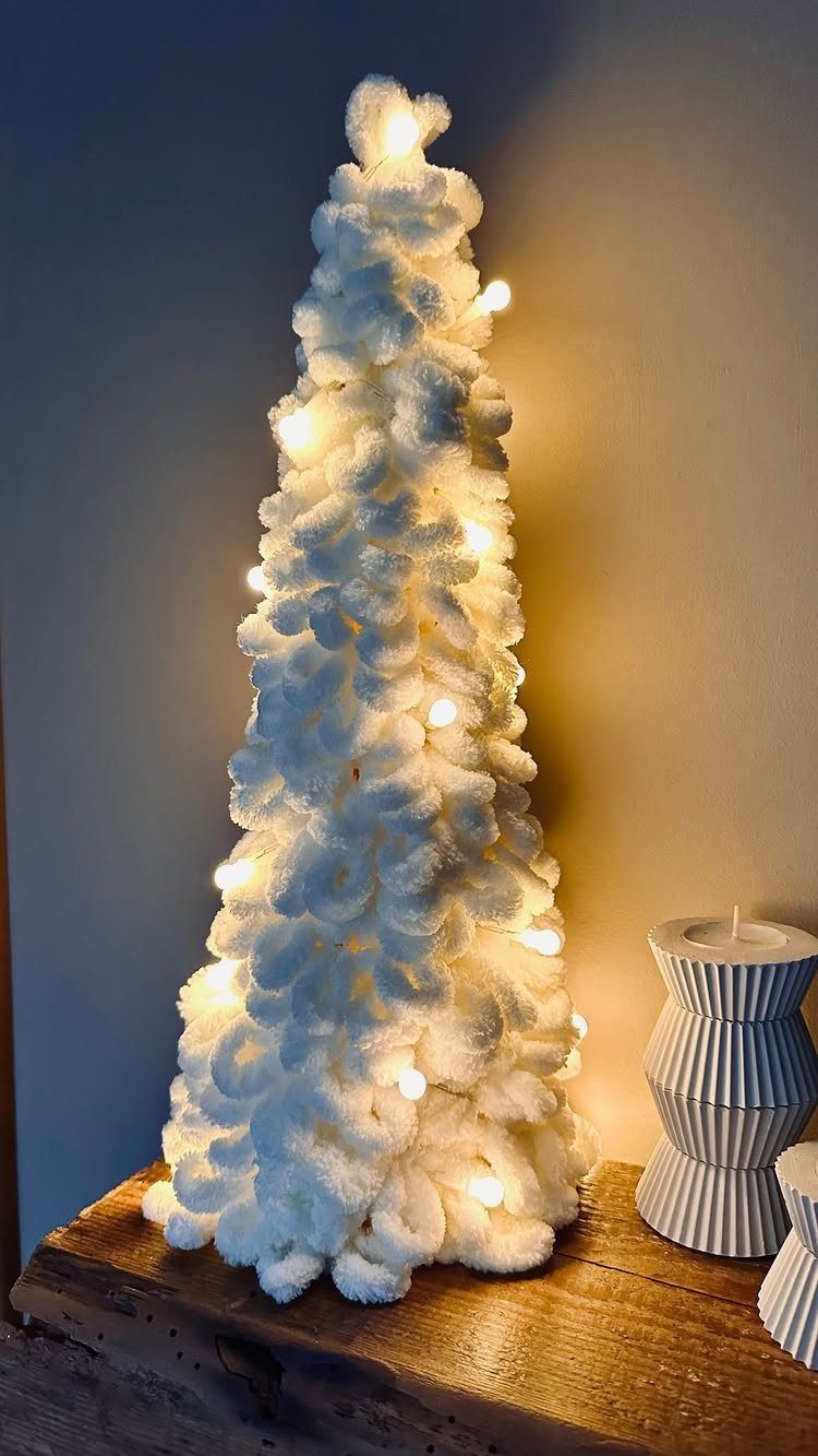 White yarn Christmas tree illuminated with warm fairy lights on a wooden table.