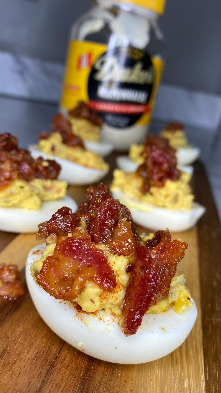 Deviled eggs topped with crispy bacon bits on a wooden cutting board