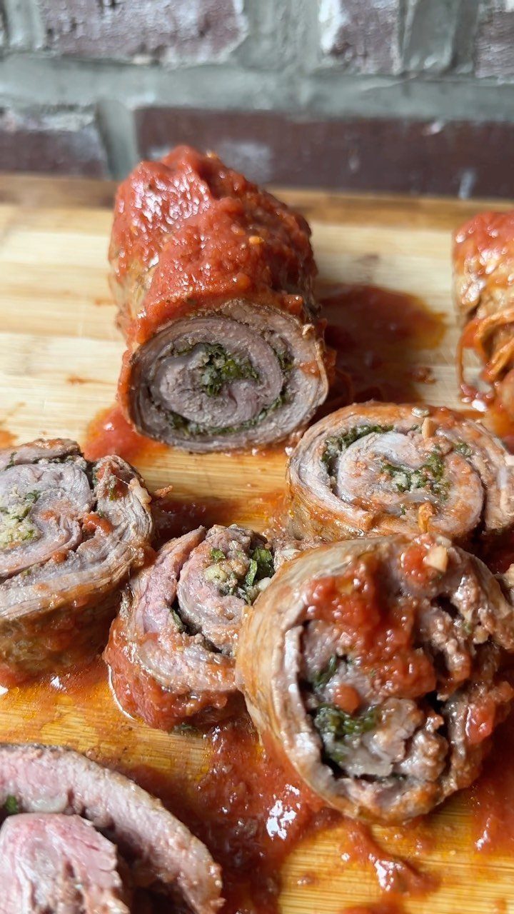 Slices of beef braciole with tomato sauce on a wooden cutting board