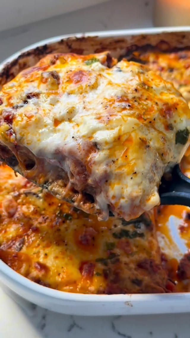 Cheesy lasagna slice lifted from a white baking dish with melted mozzarella cheese.