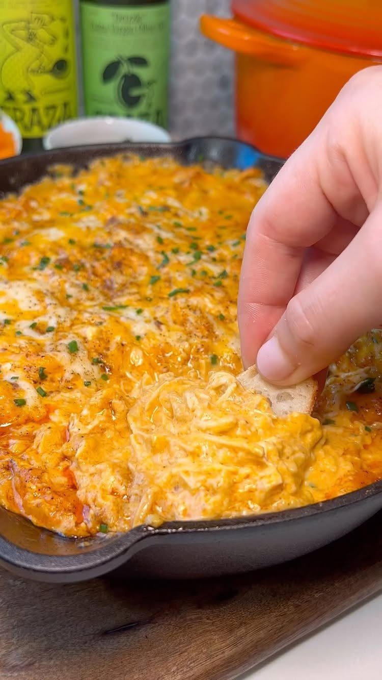 Creamy orange buffalo chicken dip in a cast iron skillet with bread dip.