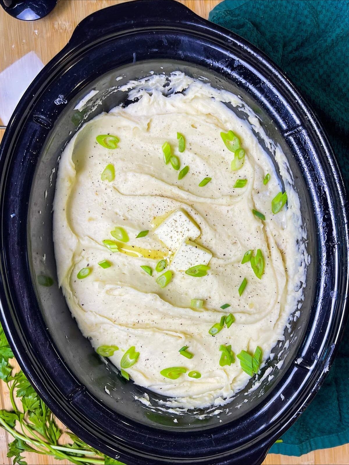 Creamy mashed potatoes in a slow cooker topped with butter and green onions