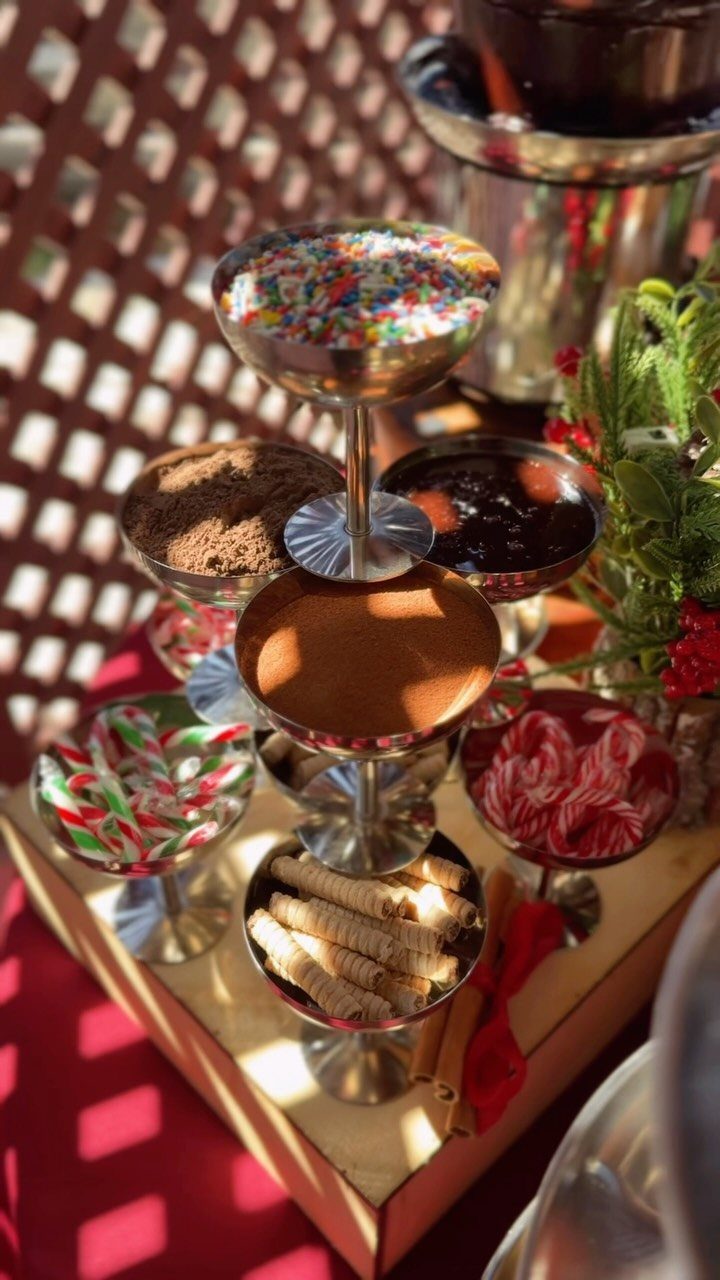 Tiered silver stand with dessert toppings and candy canes next to chocolate fountain