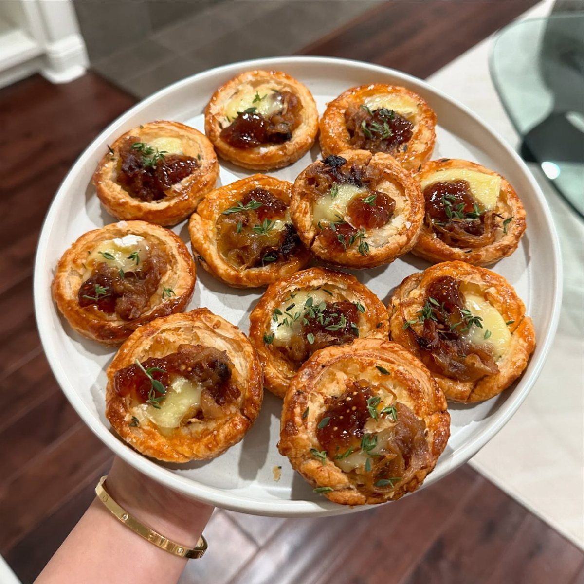 Small pastry tartlets with caramelized onions and melted cheese on a white plate.