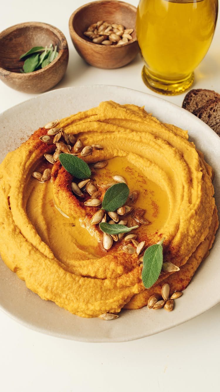 Butternut squash hummus in a white bowl topped with seeds and sage leaves.