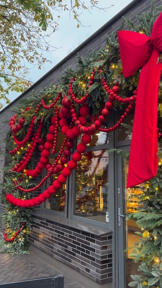 Evergreen garlands with red bead drapes and a large red bow framing a door.