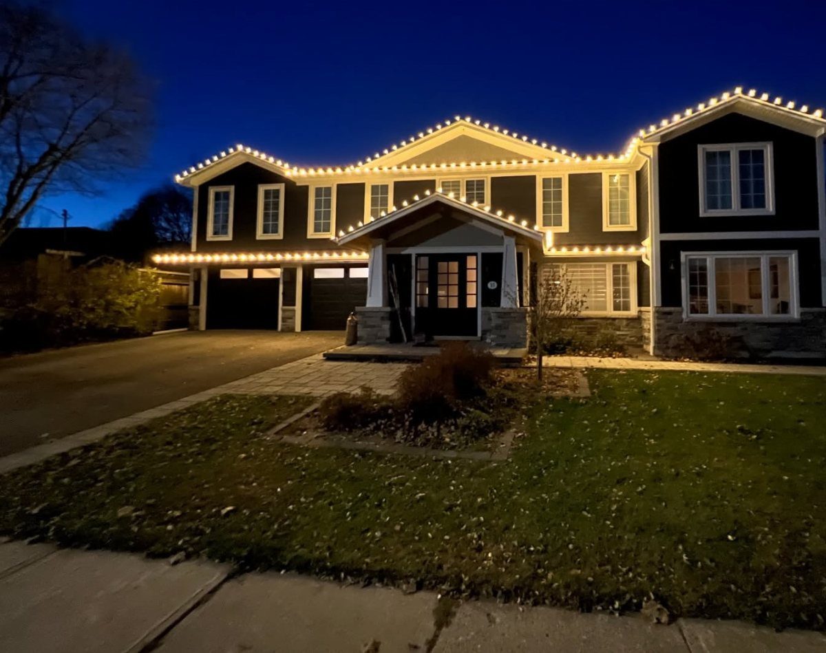 Dark grey house with warm white Christmas lights lining the roof and eaves.