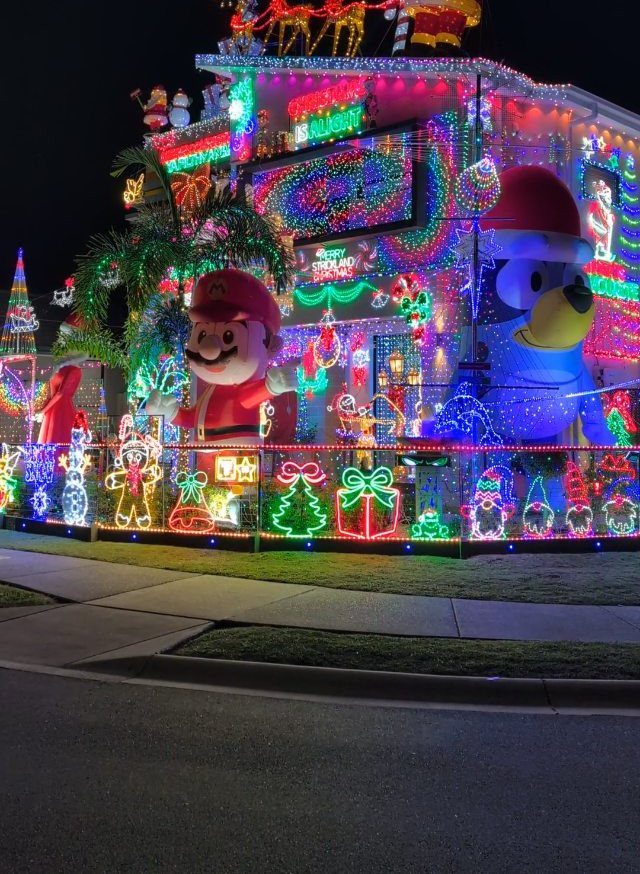 House exterior decorated with colorful Christmas lights and large character inflatables at night.