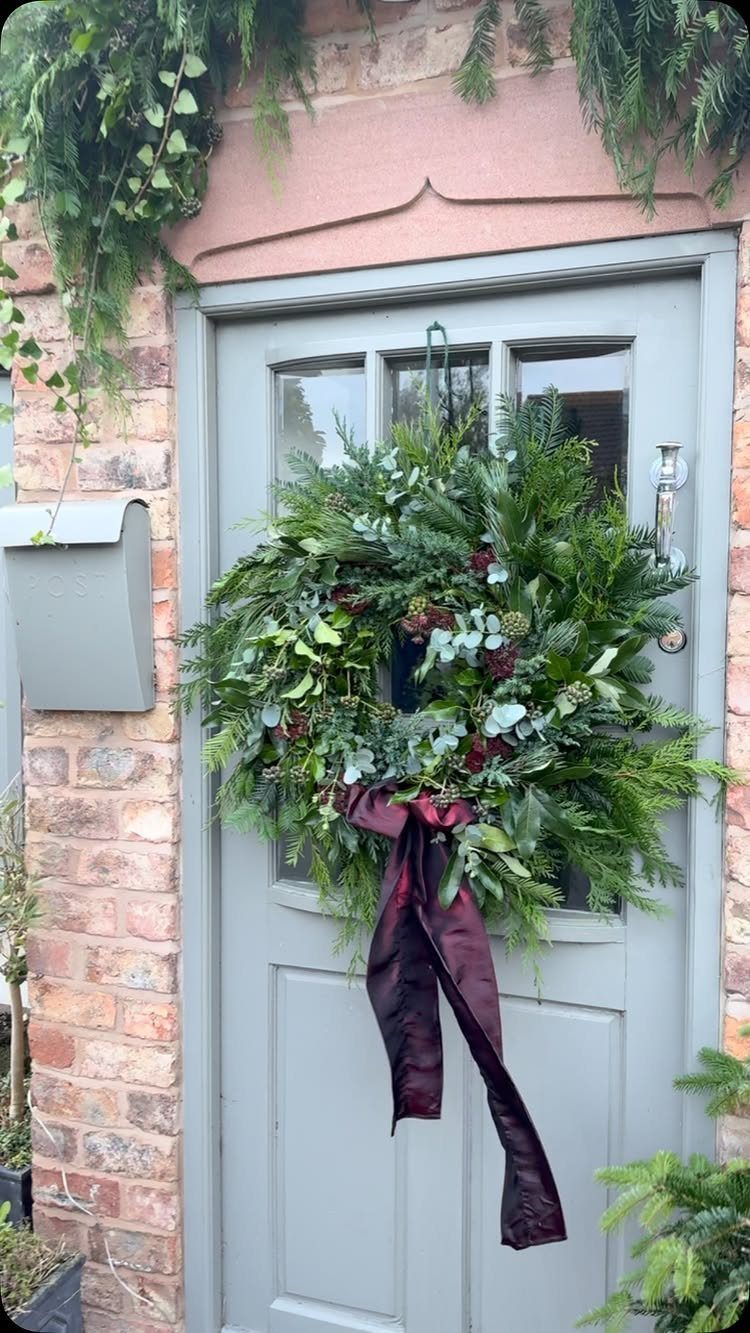 Green evergreen wreath with a red ribbon hanging on a grey front door