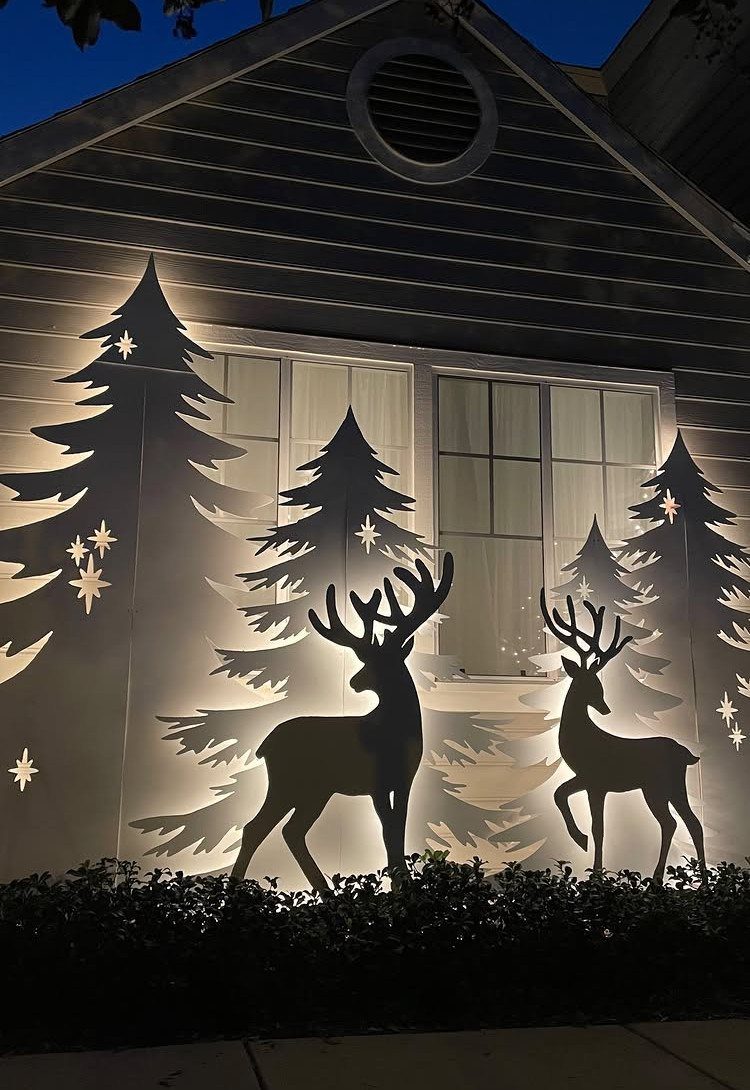 Illuminated white reindeer and pine tree silhouettes decorating a house front at night