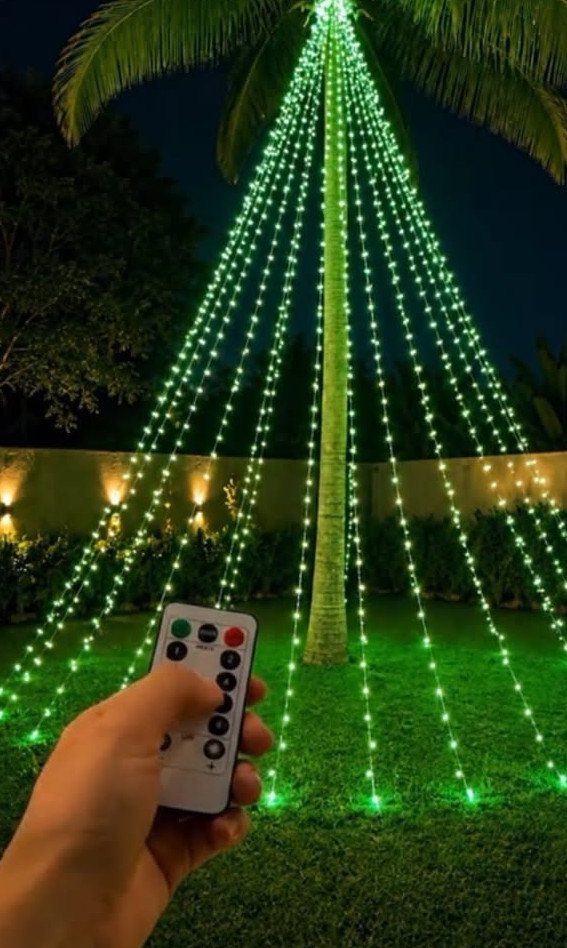 Palm tree decorated with green LED string lights in a grassy yard at night.