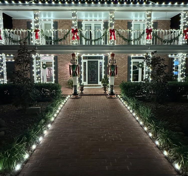 Brick house front yard decorated with nutcrackers, white lights, and festive garlands.