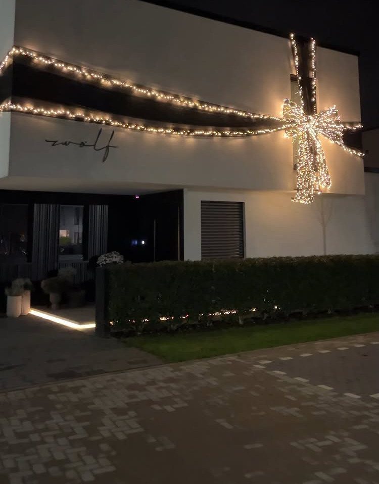 Modern white house facade decorated with glowing white Christmas lights in a bow shape.