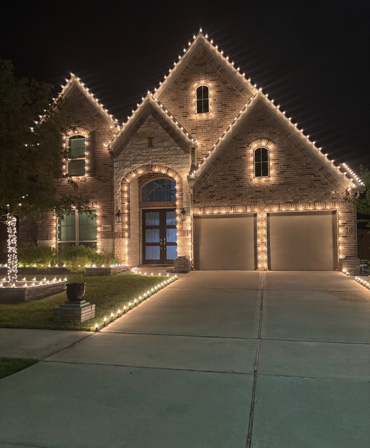 Brick house exterior decorated with warm white Christmas lights on roof and driveway