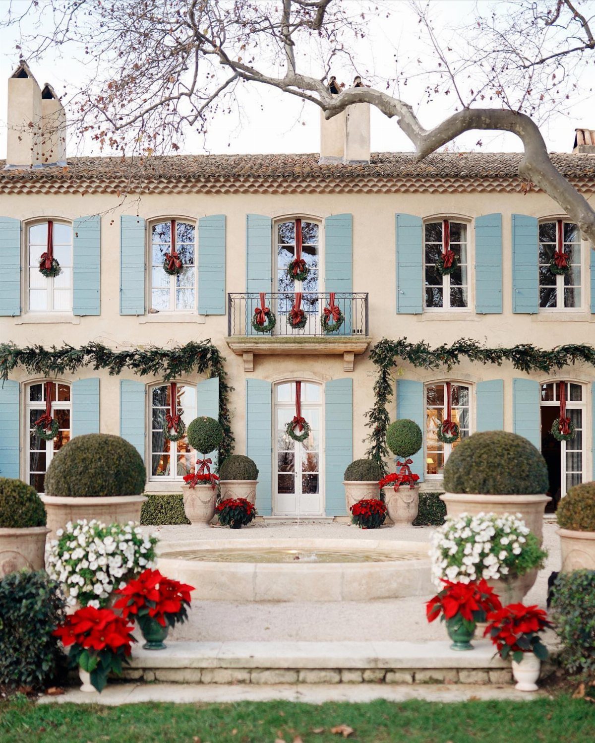 Beige house with light blue shutters and Christmas wreaths in every window.