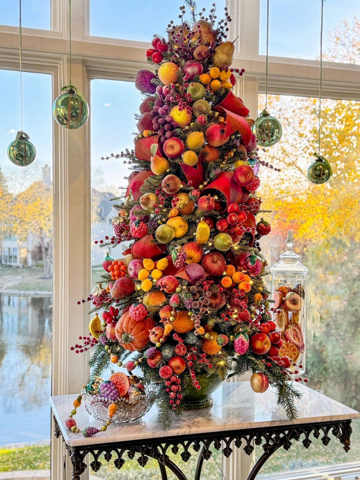 Conical fruit arrangement with apples and berries on a marble table by a window