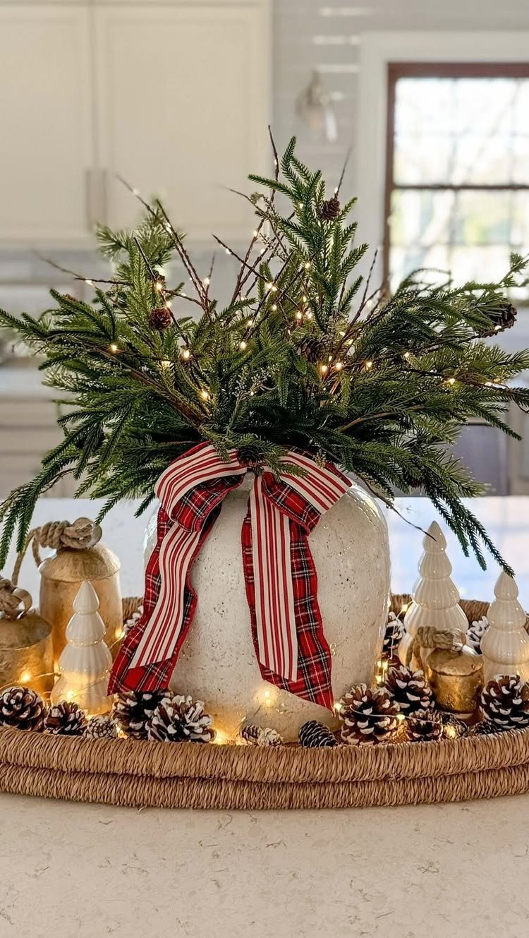 Evergreen branches with fairy lights in a white vase tied with plaid ribbon.