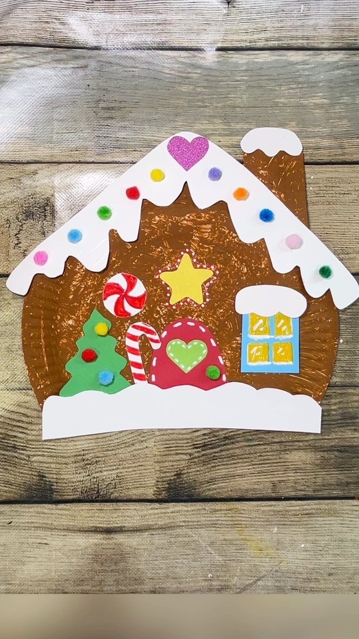Handmade gingerbread house craft with colorful pom-poms on a rustic wooden background