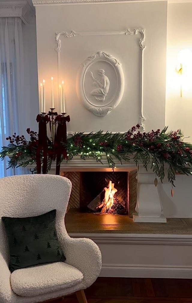 Fireplace mantel decorated with evergreen garland, red berries, and a lit red candelabra.