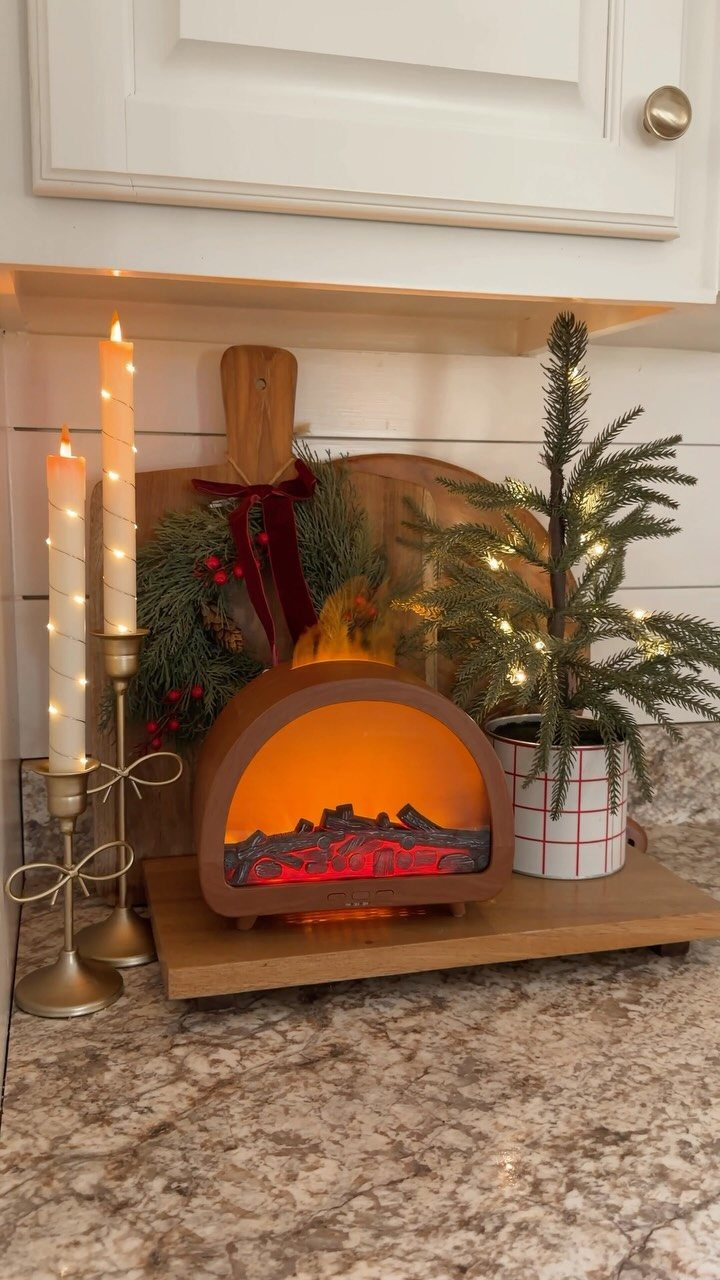 Mini evergreen tree and electric fireplace on a kitchen counter with festive decorations.