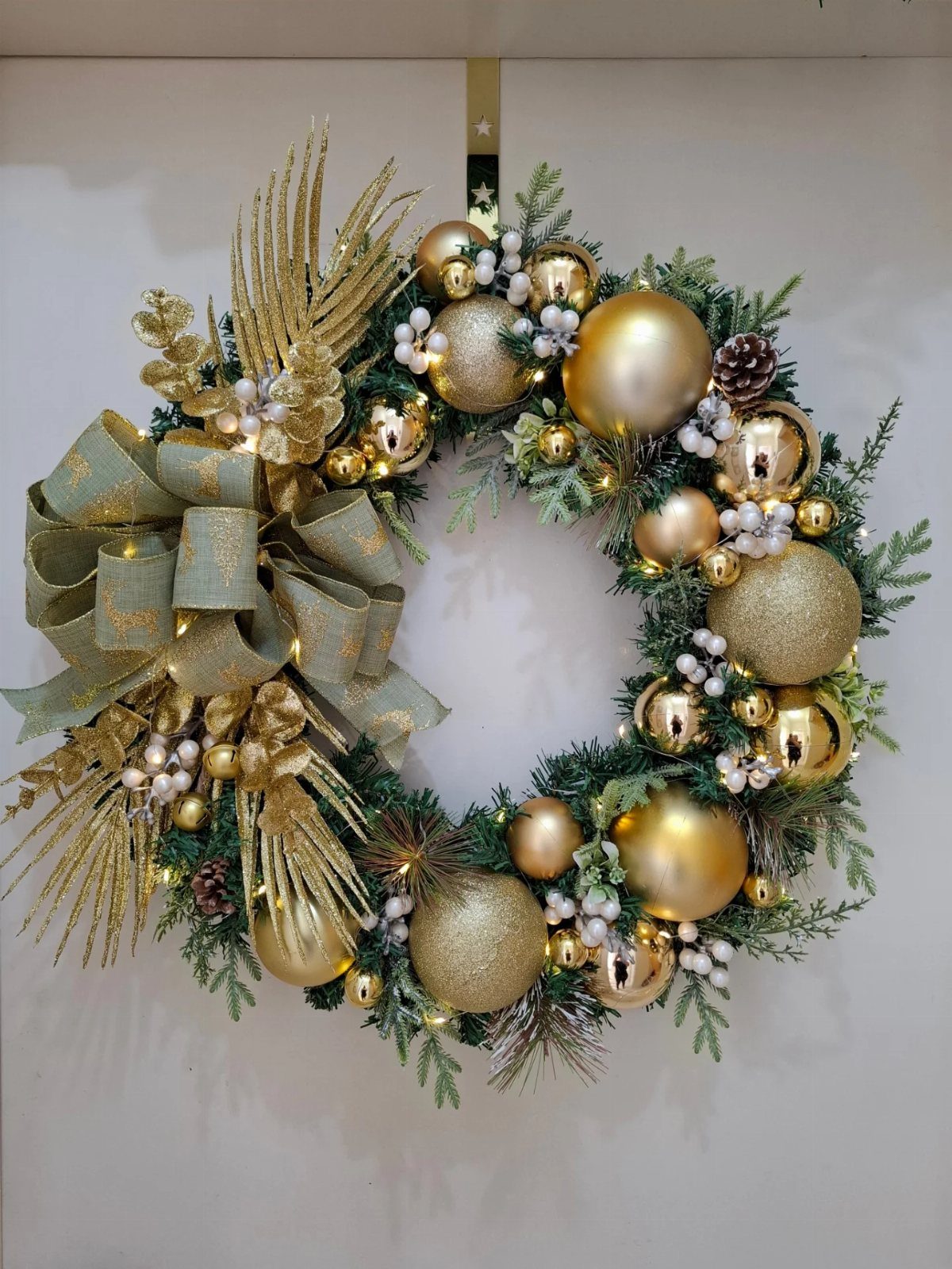 Christmas wreath with gold ornaments, white berries, and a large sage green bow.