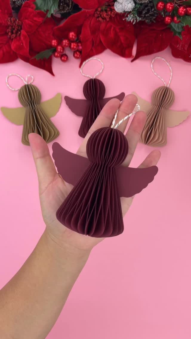 Hand holding a burgundy pleated paper angel ornament among other colorful angel ornaments.