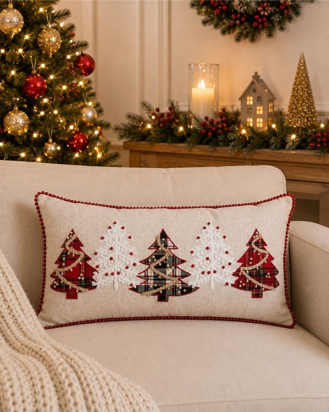 Festive cushion with embroidered Christmas trees on a cream sofa in a decorated room.