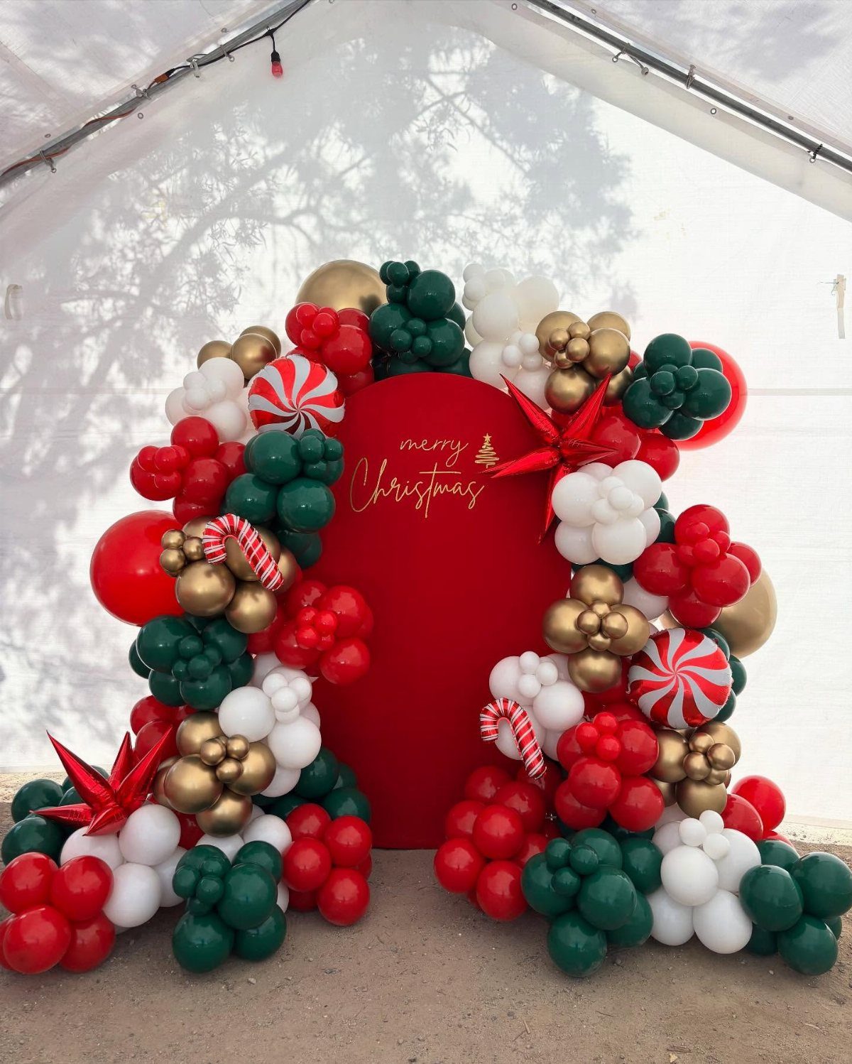 Christmas balloon garland in red, green, and gold framing a red backdrop.