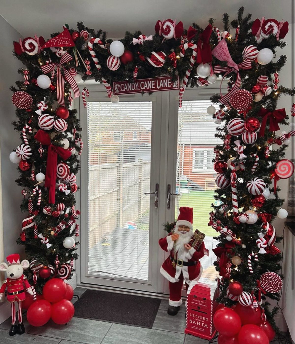 Christmas doorway decorated with candy cane themed garland, red balloons, and Santa figure