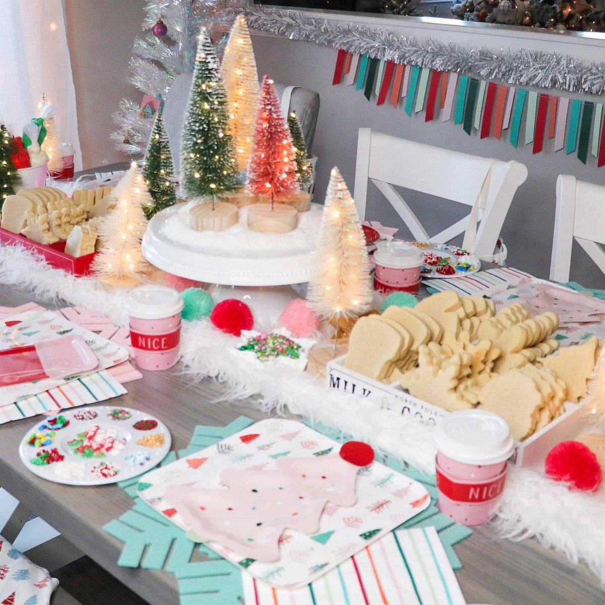 Christmas cookie decorating station with tree-shaped cookies, mini lit trees, and colorful sprinkles.