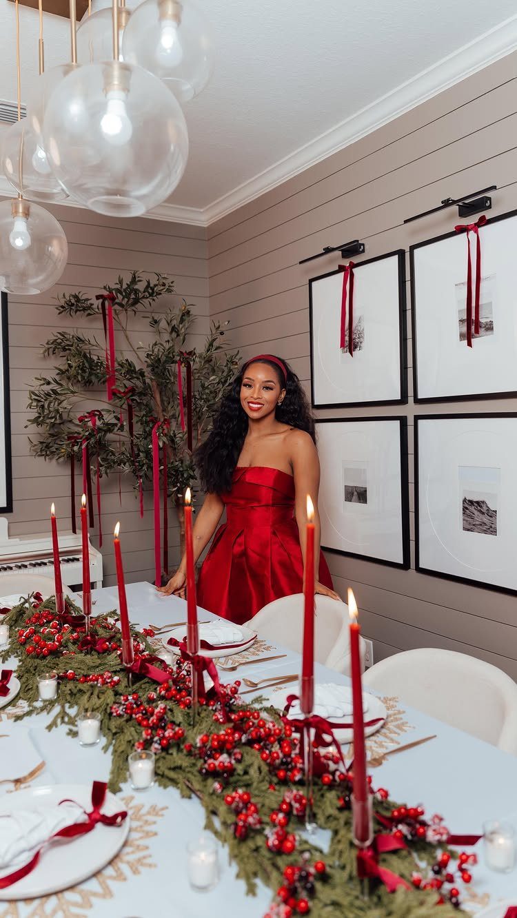 Woman in red dress standing behind a festive Christmas dinner table with red candles.