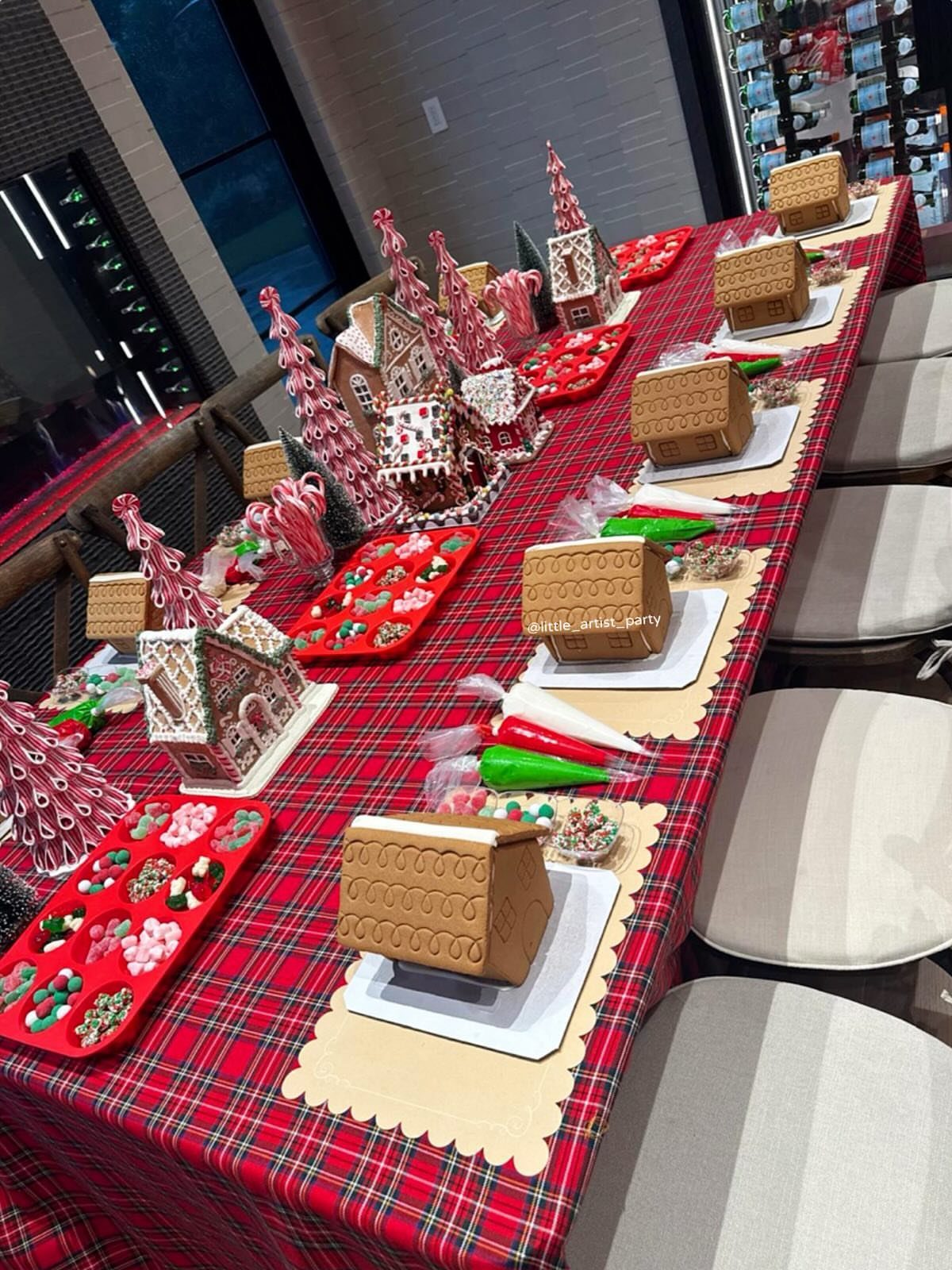 Gingerbread houses and decorating supplies arranged on a red plaid tablecloth.