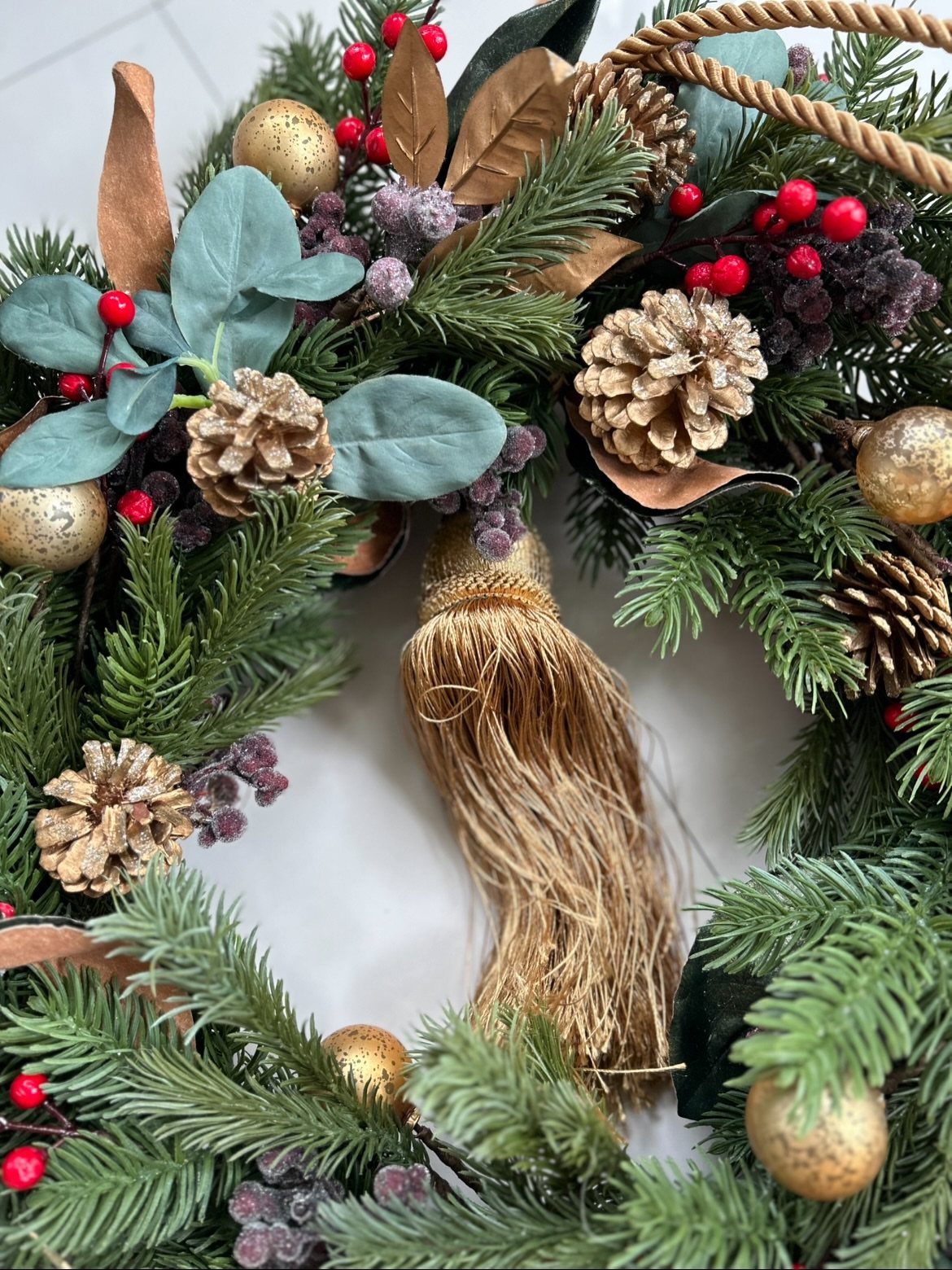 Christmas wreath with pinecones, red berries, gold ornaments, and a gold tassel.
