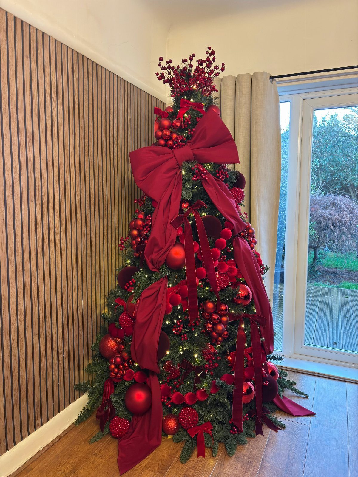 Christmas tree decorated with red faux flowers, large red velvet bows, and red ornaments.