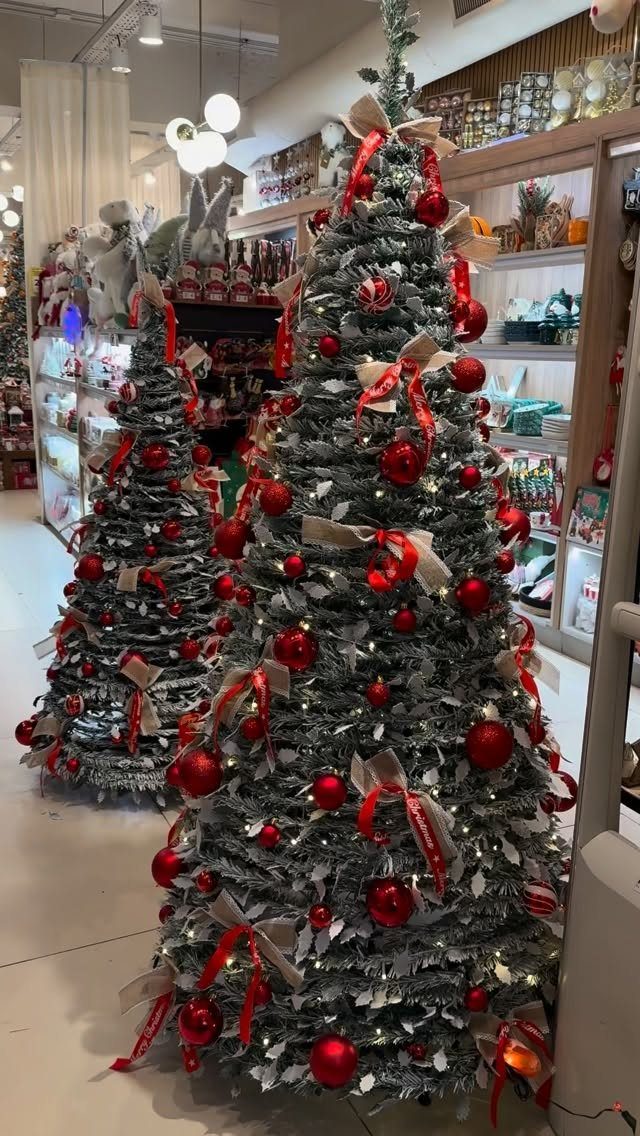 Flocked Christmas trees decorated with red ornaments and silver tinsel in a store.