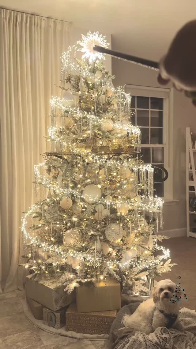 White and gold decorated Christmas tree with warm lights and a small white dog.