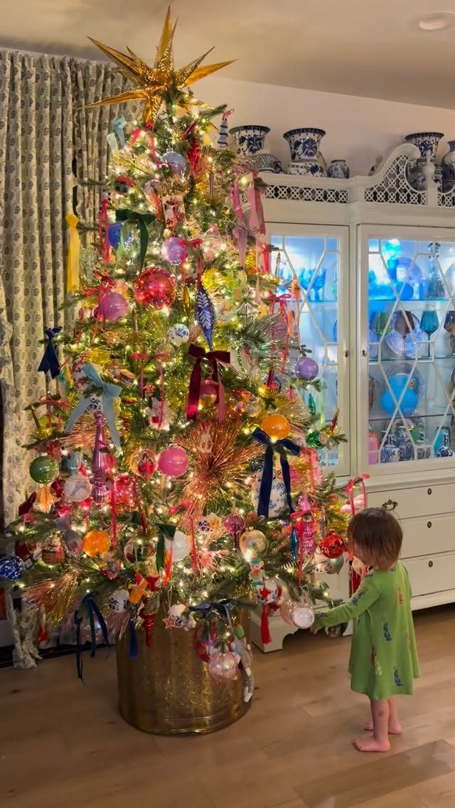 Densely decorated multicolored Christmas tree with a gold star and a small child.