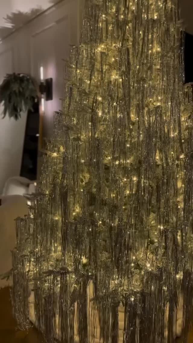 Silver tinsel Christmas tree glowing with warm white fairy lights in a room