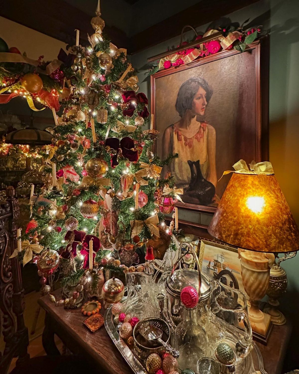 Ornate Victorian style Christmas tree with gold ornaments and red ribbons beside a portrait.