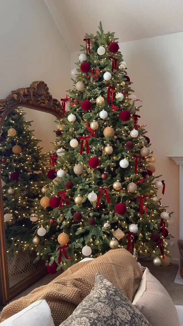 Decorated Christmas tree with red ribbons and gold ornaments reflected in a gold mirror.